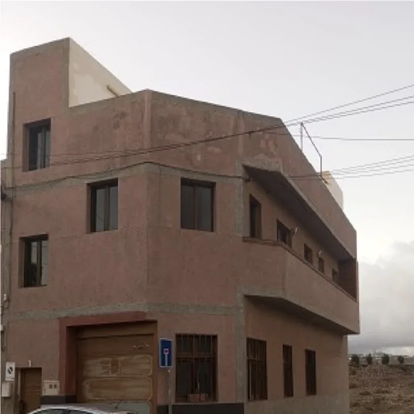 Edificio de esquina con la fachada envejecida en tono rosado antes de pintar, en Gran Canaria