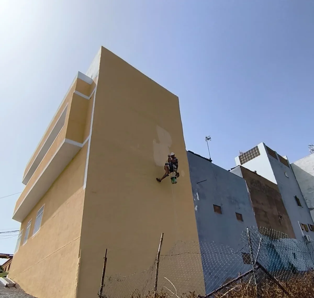 Técnico de ESS Canarias descolgado con cuerda pintando la medianera de un edificio en Gran Canaria